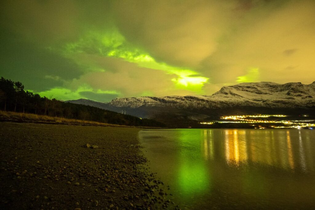 Northern lights over the lake at Abisko, village lights on the far shore
